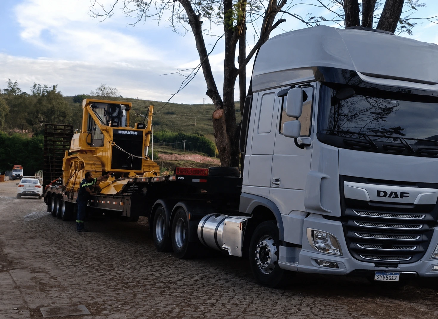 Caminhão prancha transportando máquina pesada em operação externa